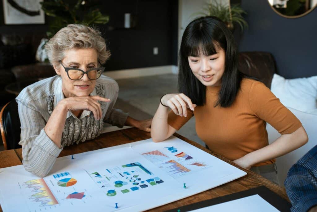 Two women discussing charts at a modern office desk, showcasing business collaboration. v4 Ways Veteran Coaching Can Transform Your Business Strategy as a Female Entrepreneur