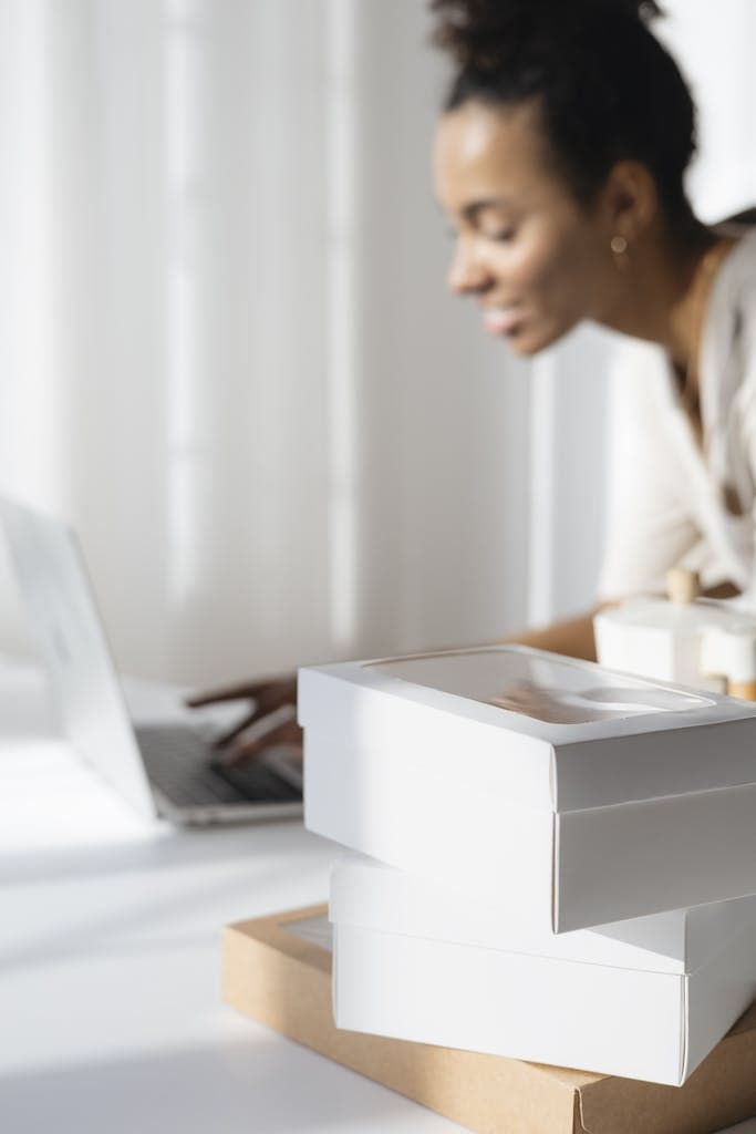 A focused woman planning her bakery business with a laptop and packaging boxes. Why Hiring a Business Coach for Small Businesses Might Be the Smartest Move You Make