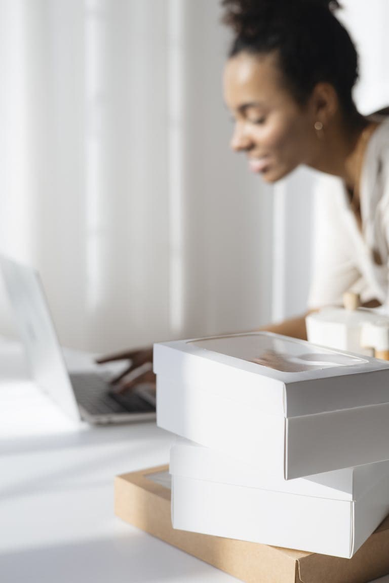 A focused woman planning her bakery business with a laptop and packaging boxes. Why Hiring a Business Coach for Small Businesses Might Be the Smartest Move You Make