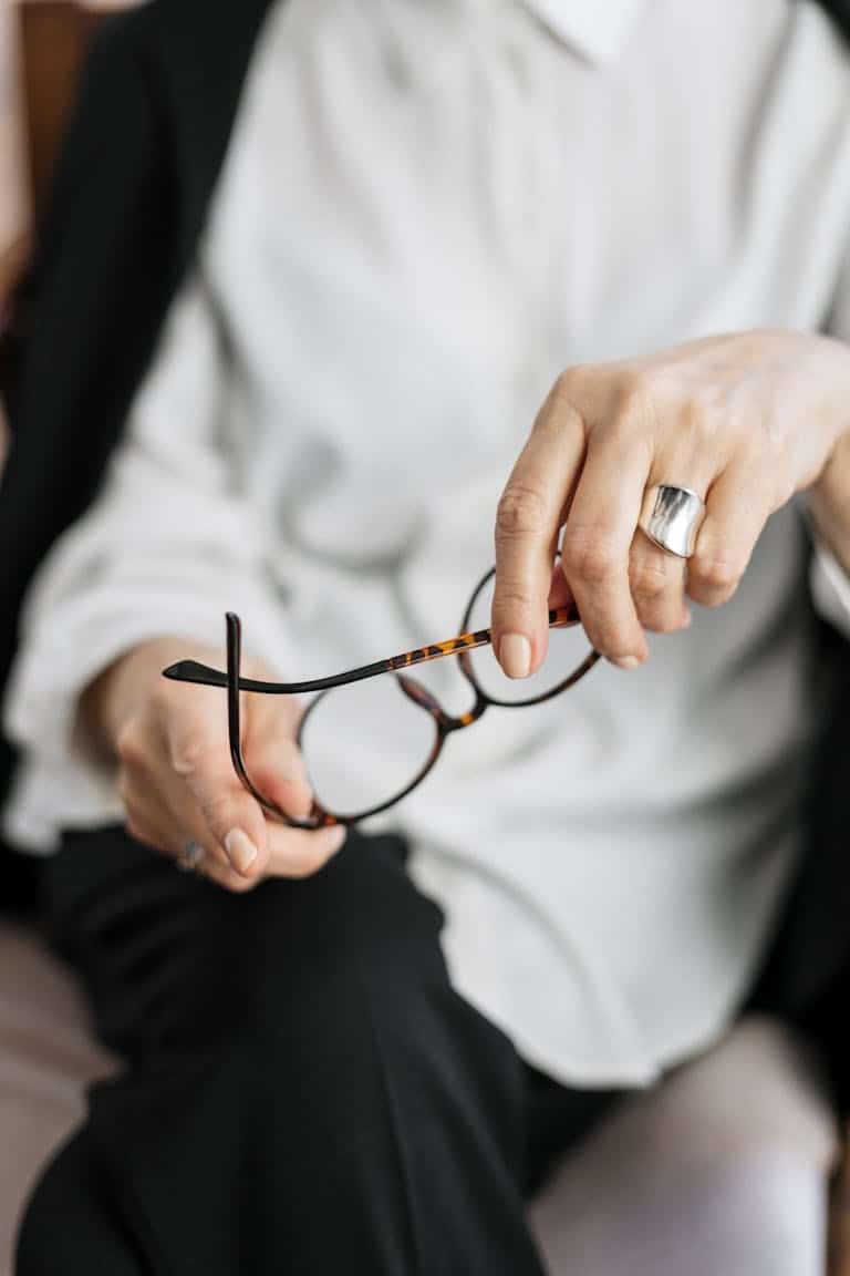Close-up of a woman holding glasses, symbolizing thought and professionalism. How a Female Business Coach Helps You Scale Smarter (Not Harder)