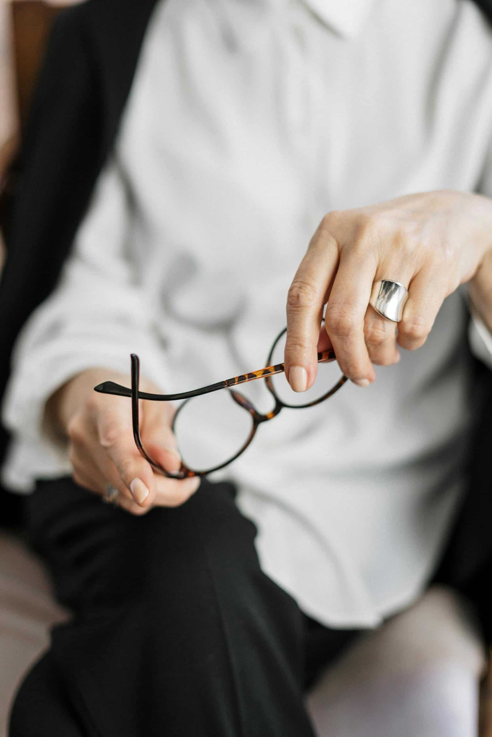 Close-up of a woman holding glasses, symbolizing thought and professionalism. How a Female Business Coach Helps You Scale Smarter (Not Harder)
