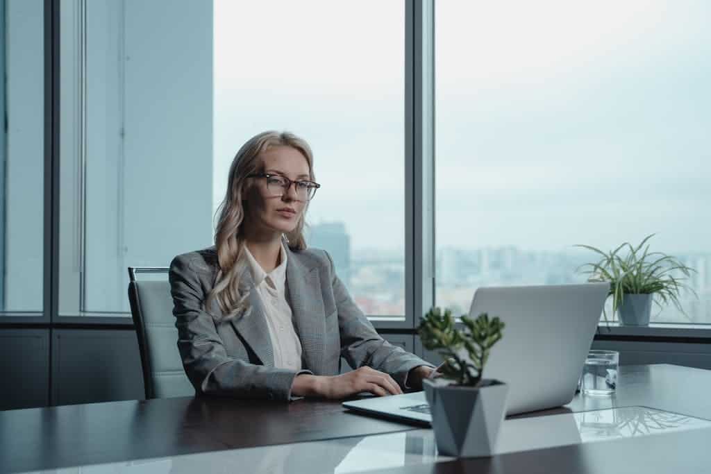 A confident businesswoman in a grey suit working on a laptop in a modern office setting. Fraactional CMO Digital strategies for small business growth