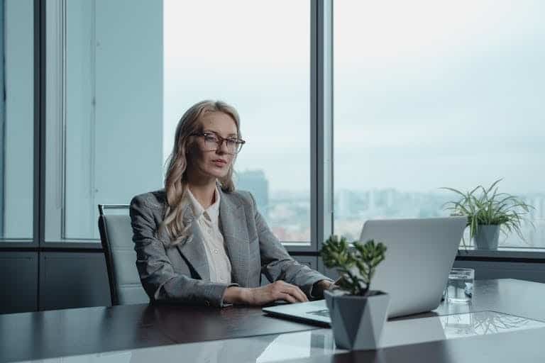 A confident businesswoman in a grey suit working on a laptop in a modern office setting. Fraactional CMO