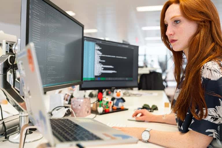 A focused female software engineer coding on dual monitors in a modern office. Why SEO Alone Won’t Save You (But Systems Will)