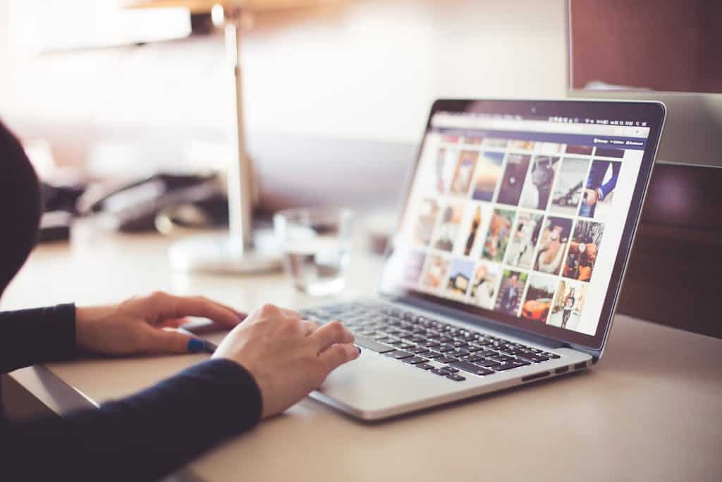 Close-up of hands typing on a laptop with an image gallery open on the screen. Content conversion