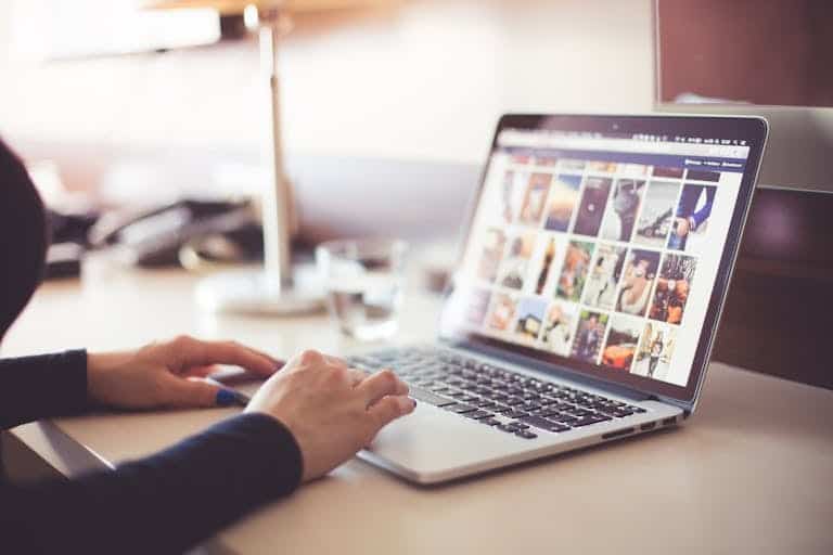 Close-up of hands typing on a laptop with an image gallery open on the screen. Content conversion