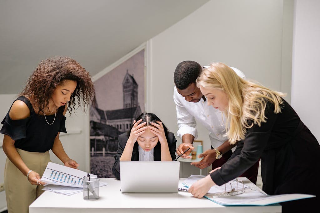 Diverse group of coworkers engaged in a collaborative office meeting, discussing around a laptop. Stop Winging it - Brand Communication