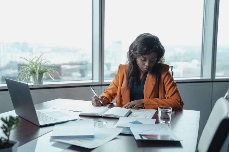Focused black businesswoman analyzing documents at an office desk with city view. Fractional CMO