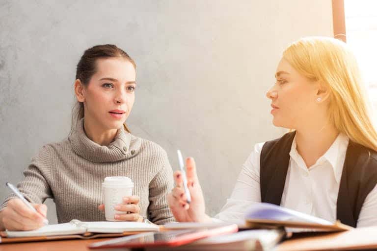 Two women engaging in a professional conversation over coffee and notes. Fractional CMO Agency or Solo