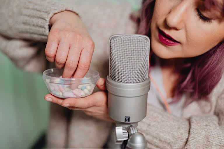 Woman in studio setting recording vlog, holding pills near microphone for ASMR content.