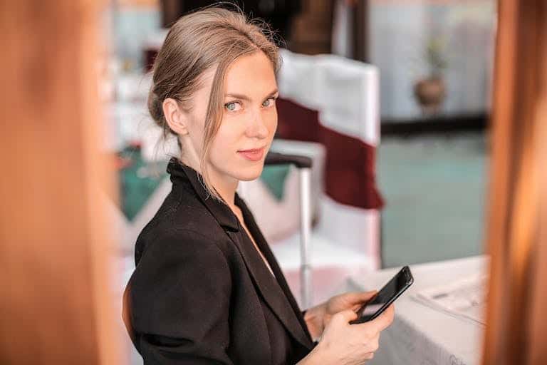Young businesswoman using smartphone indoors with confident expression. Modern and professional setting. Fractional CMO