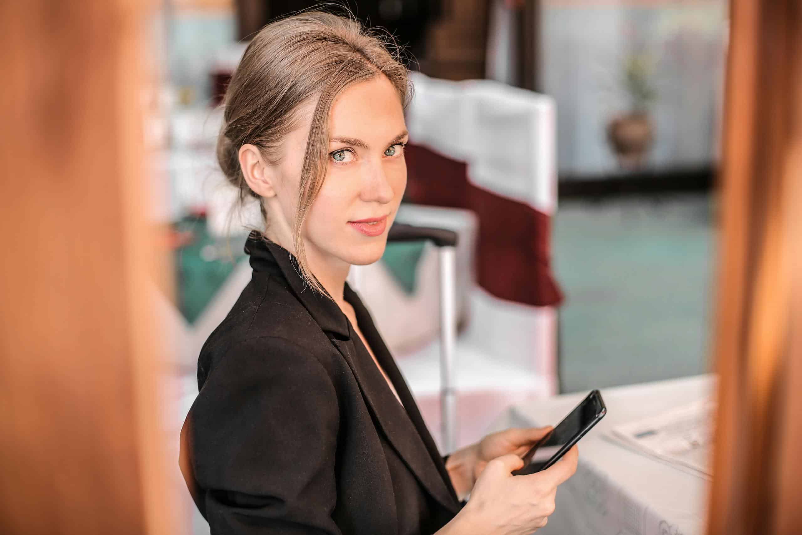 Young businesswoman using smartphone indoors with confident expression. Modern and professional setting. Fractional CMO