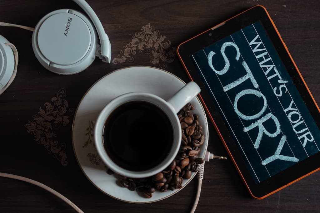 Flat lay of coffee cup, headphones, and tablet with 'What's Your Story' on screen. Digital Brand Storytelling