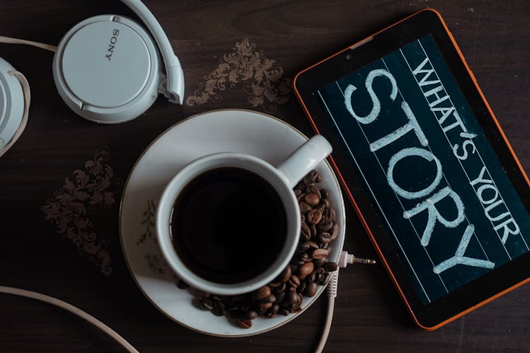 Flat lay of coffee cup, headphones, and tablet with 'What's Your Story' on screen. Digital Brand Storytelling