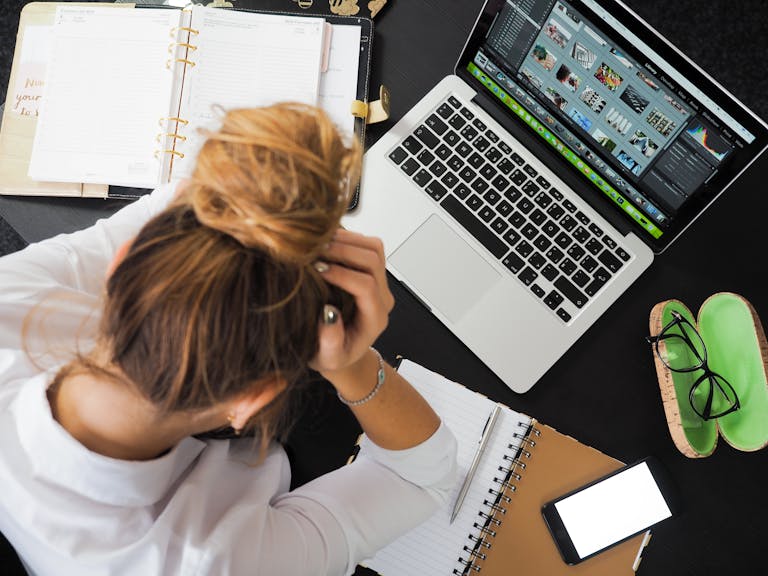Overhead view of a stressed woman working at a desk with a laptop, phone, and notebooks. Online Marketing Services for Small Business: What to Prioritize When You Can’t Do It All