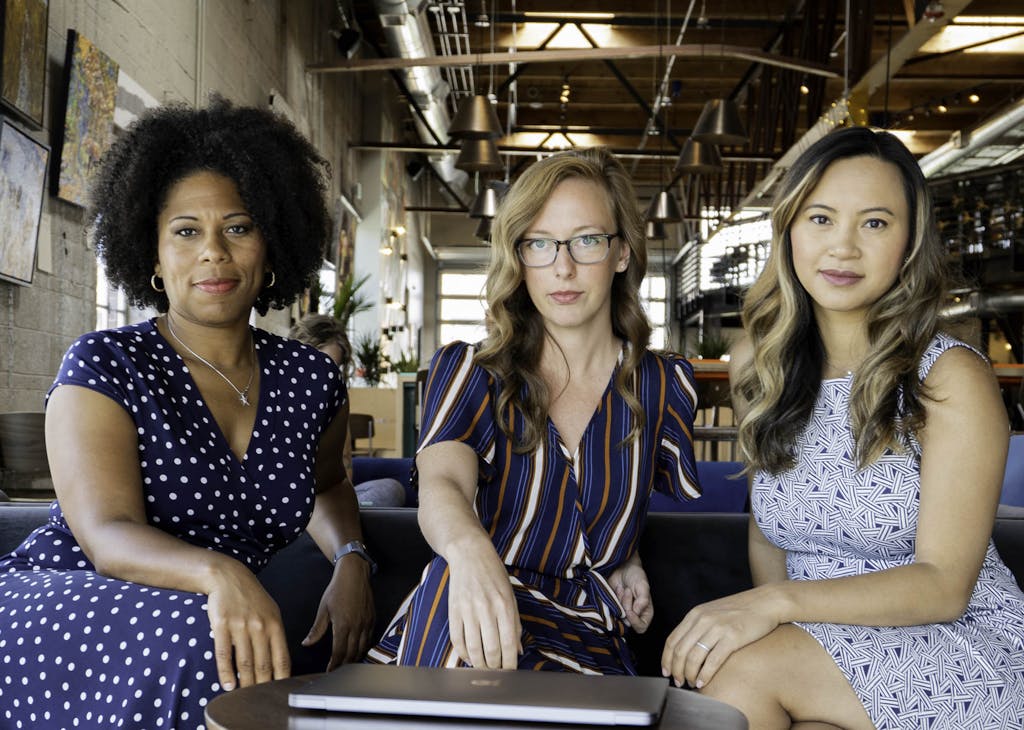 Three professional women sitting confidently in a modern office space, embracing diversity and collaboration.