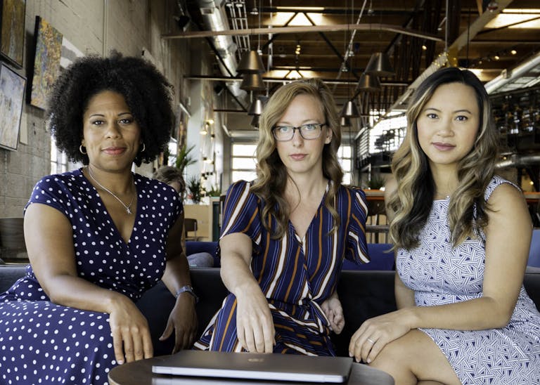Three professional women sitting confidently in a modern office space, embracing diversity and collaboration.