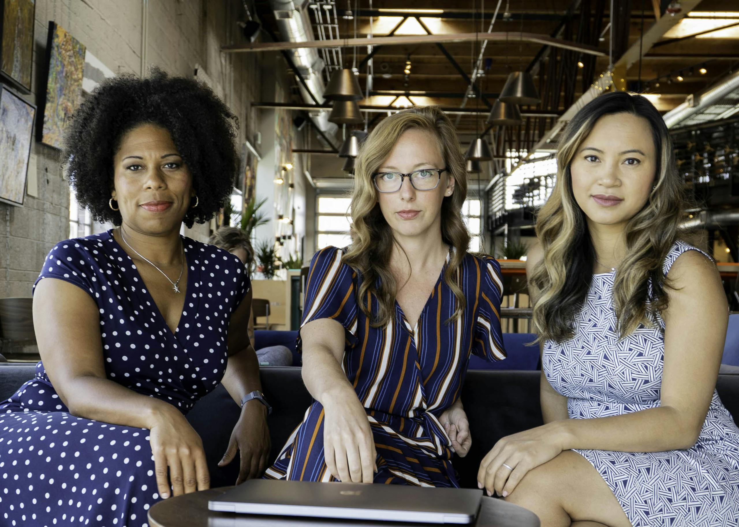 Three professional women sitting confidently in a modern office space, embracing diversity and collaboration.